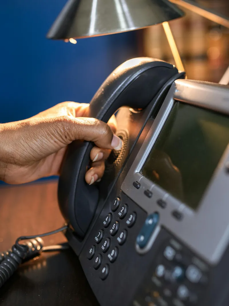A hand lifting the receiver of an office desk phone