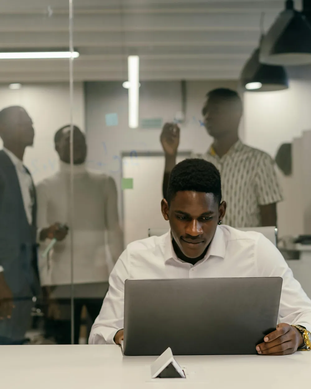 A man working on a laptop in an office while colleagues talk behind him